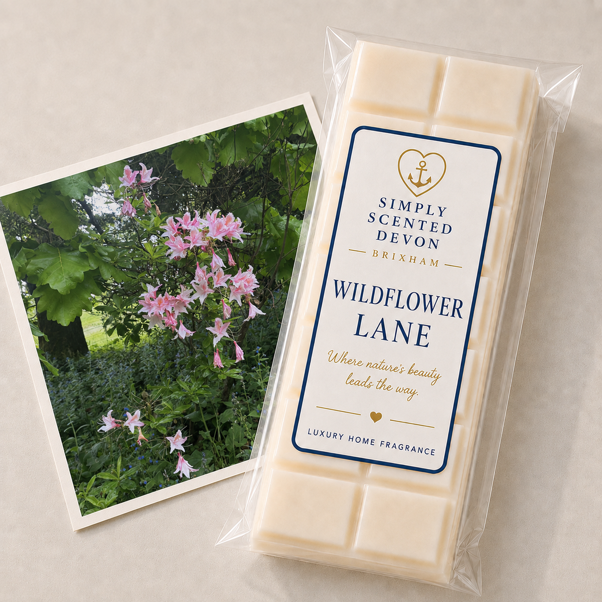 A packaged bar of Simply Scented Devon Brixham 'Wildflower Lane' luxury home fragrance wax melts, shown next to a printed photo card of pink wildflowers on a light beige surface.